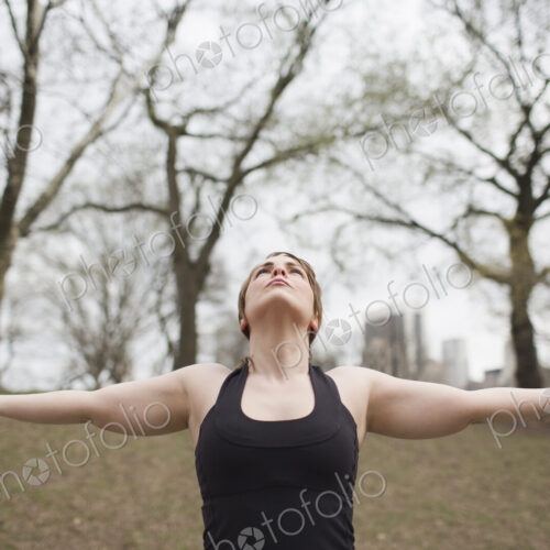 A young woman in Central Park, in a black leotard and leggings, doing yoga.