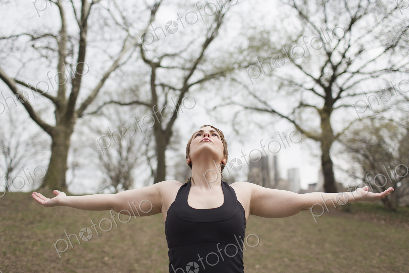 A young woman in Central Park, in a black leotard and leggings, doing yoga.