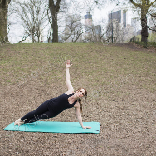 A young woman in Central Park, in a black leotard and leggings, doing yoga.