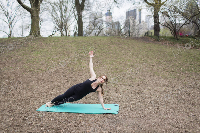 A young woman in Central Park, in a black leotard and leggings, doing yoga.