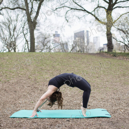 A young woman in Central Park, in a black leotard and leggings, doing yoga.