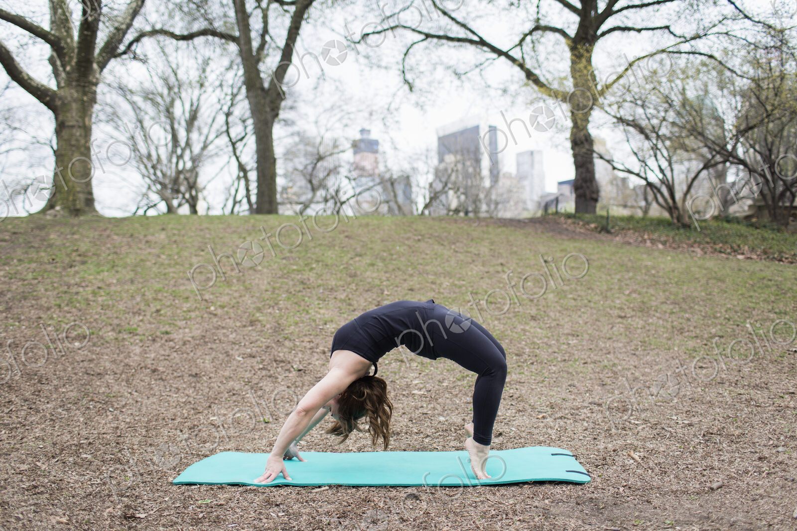 A young woman in Central Park, in a black leotard and leggings, doing yoga.