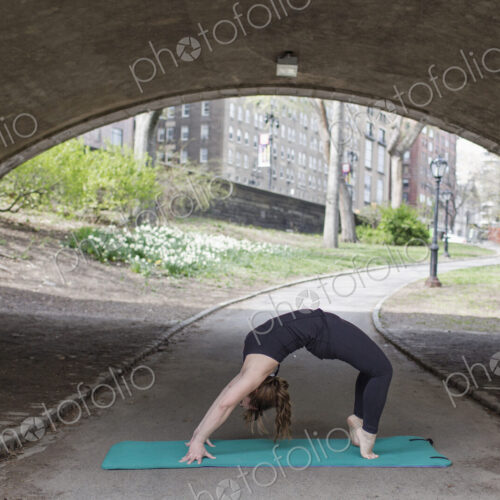 A young woman in Central Park, in a black leotard and leggings, doing yoga.