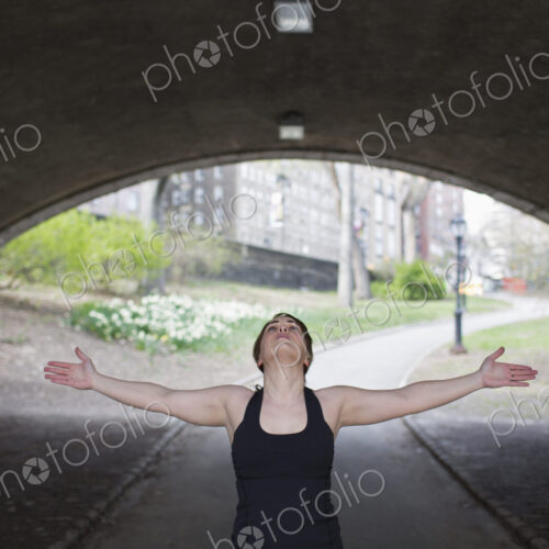 A young woman in Central Park, in a black leotard and leggings, doing yoga.