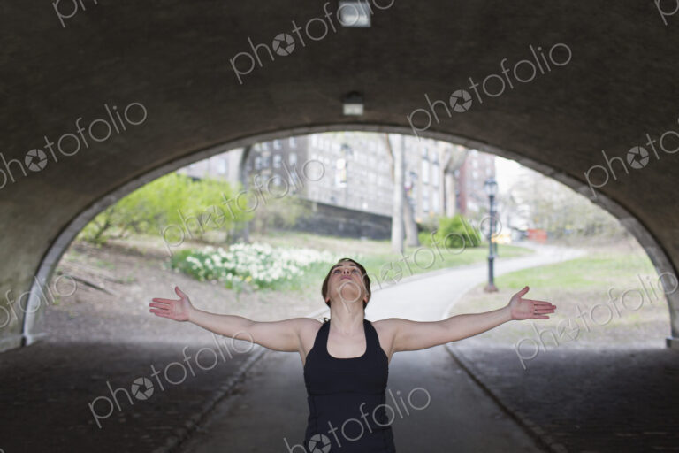 A young woman in Central Park, in a black leotard and leggings, doing yoga.