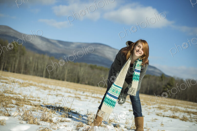 A young woman in a snowy field in a rural landscape. Scooping up snow to make a snowball.