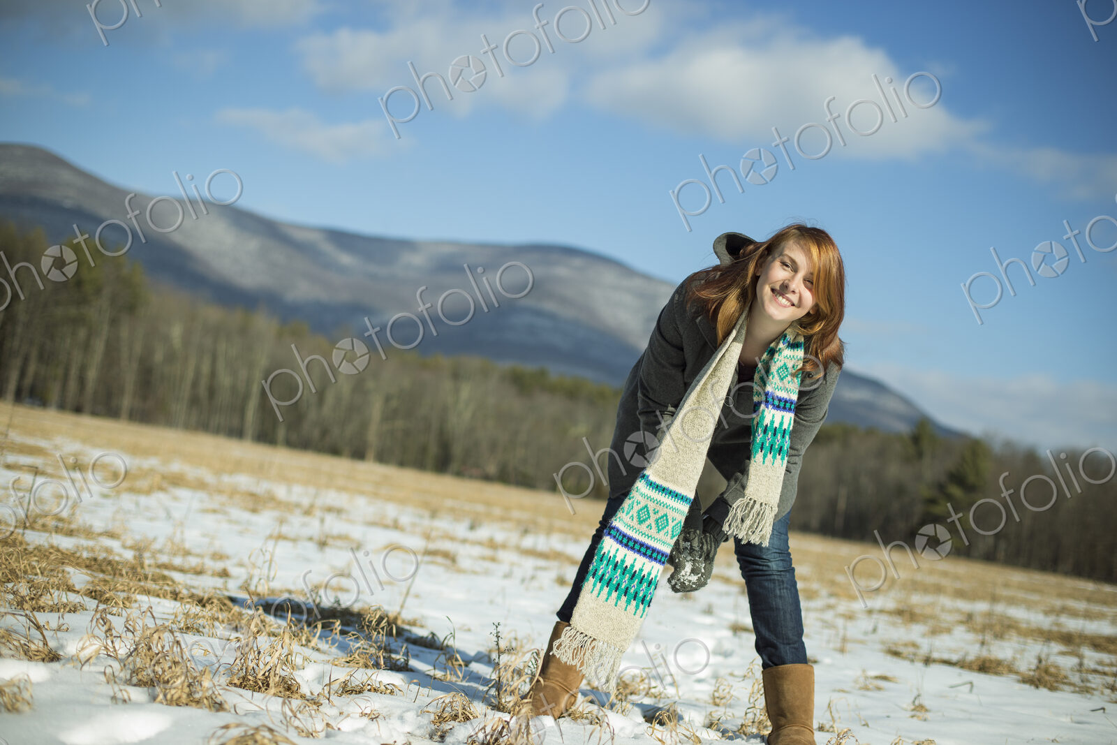A young woman in a snowy field in a rural landscape. Scooping up snow to make a snowball.