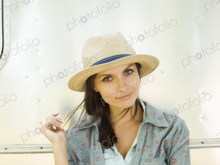 A young woman in a straw hat, her head tilted looking curious.