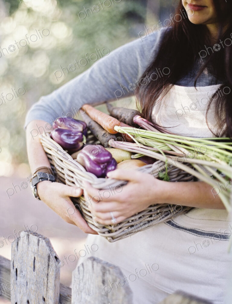 A young woman in a vegetable garden, carrying a basket with freshly harvested organic…