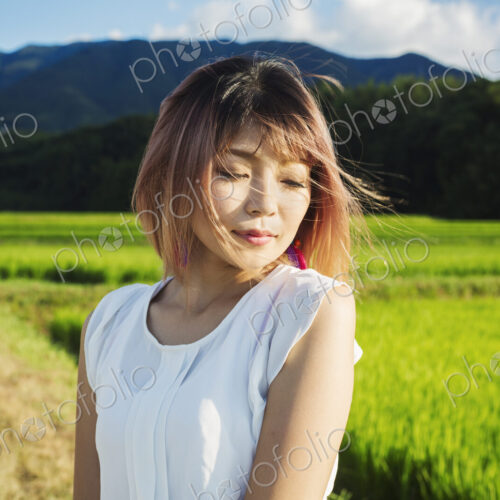 A young woman in a white shirt, hair blown in the wind, standing in open space by rice… A young woman in a white shirt, hair blown in the wind, standing in open space by rice…