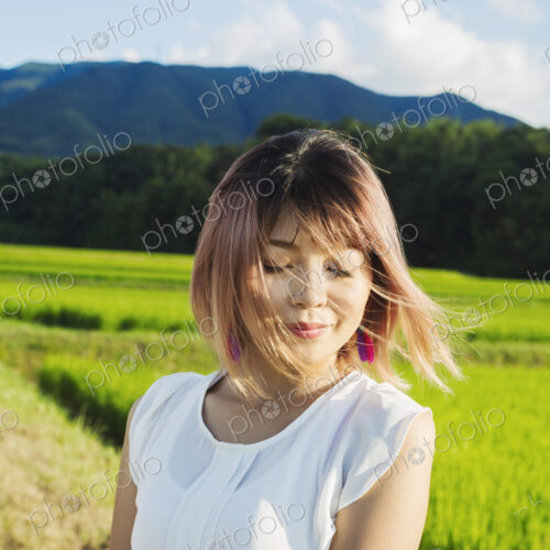 A young woman in a white shirt, hair blown in the wind, standing in open space by rice… A young woman in a white shirt, hair blown in the wind, standing in open space by rice…
