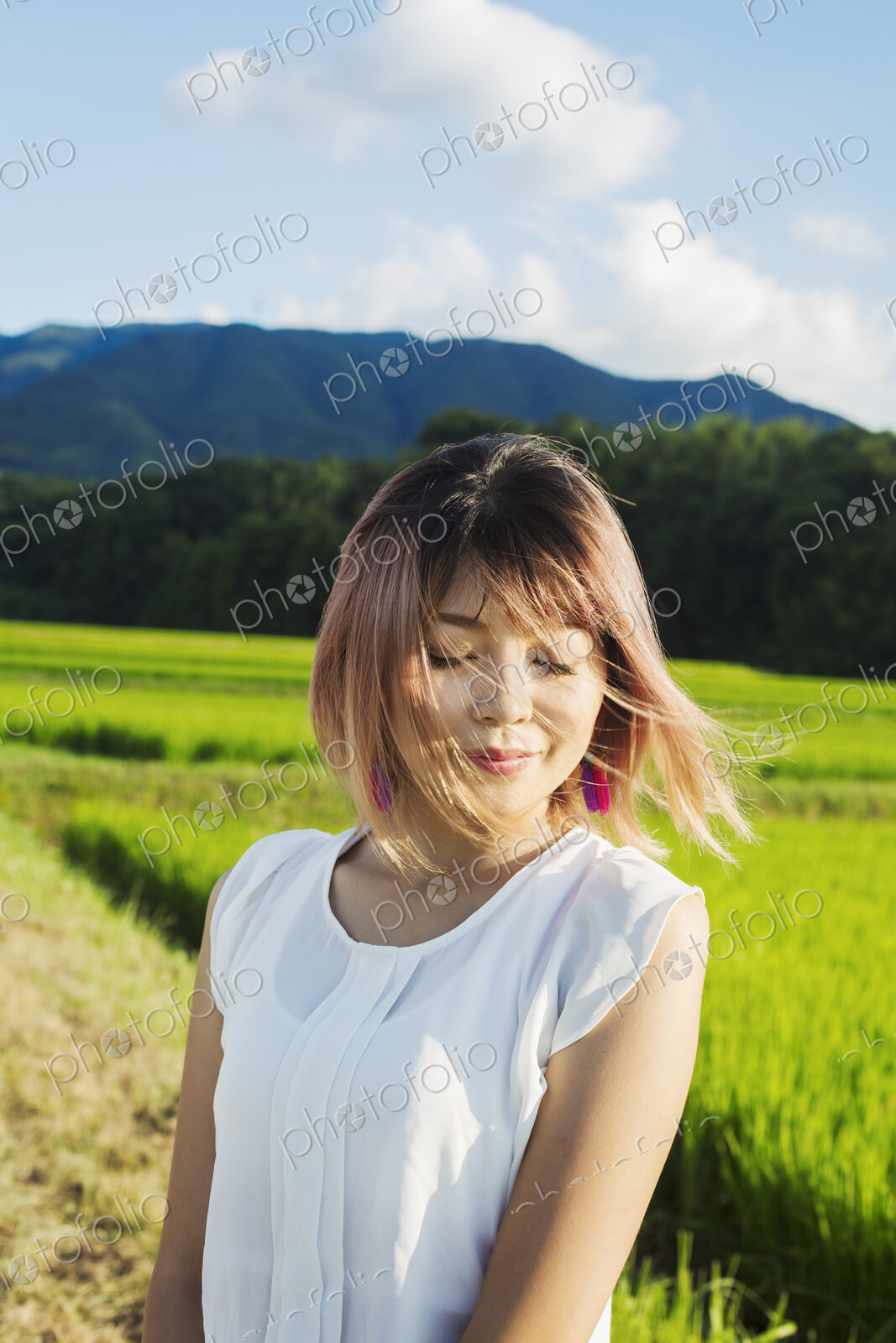 A young woman in a white shirt, hair blown in the wind, standing in open space by rice…
