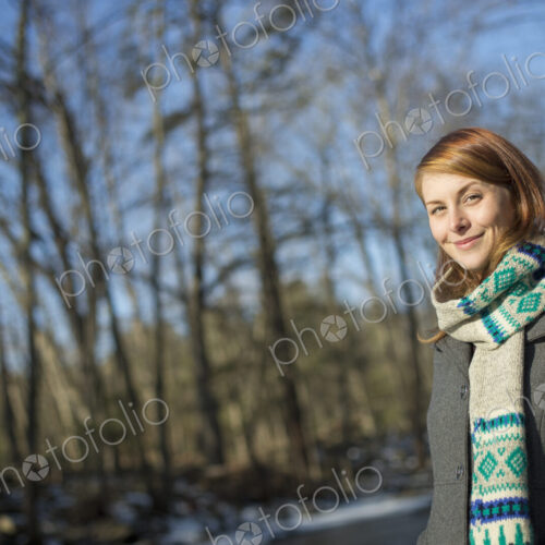 A young woman in a woodland on a winter day. Wearing a bright knitted patterned scarf. A young woman in a woodland on a winter day. Wearing a bright knitted patterned scarf.