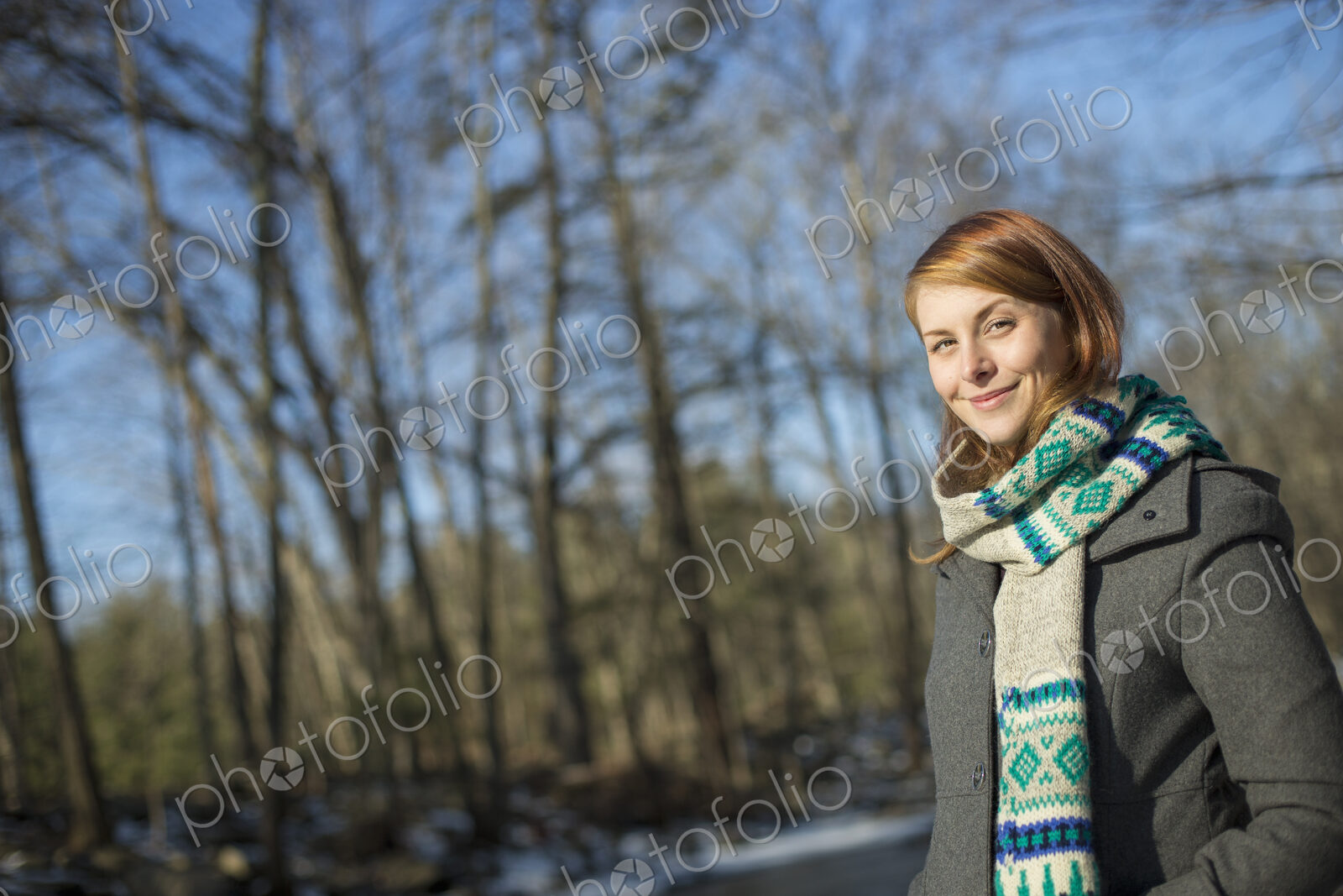 A young woman in a woodland on a winter day. Wearing a bright knitted patterned scarf.