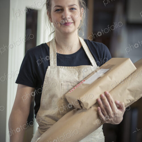 A young woman in a workshop, holding two packages wrapped in brown packaging paper,… A young woman in a workshop, holding two packages wrapped in brown packaging paper,…