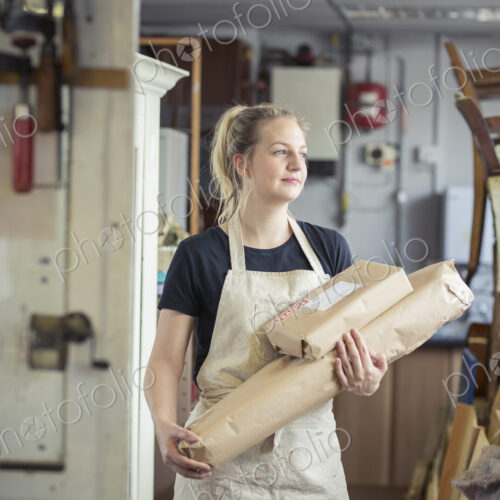 A young woman in a workshop, holding two packages wrapped in brown packaging paper,… A young woman in a workshop, holding two packages wrapped in brown packaging paper,…
