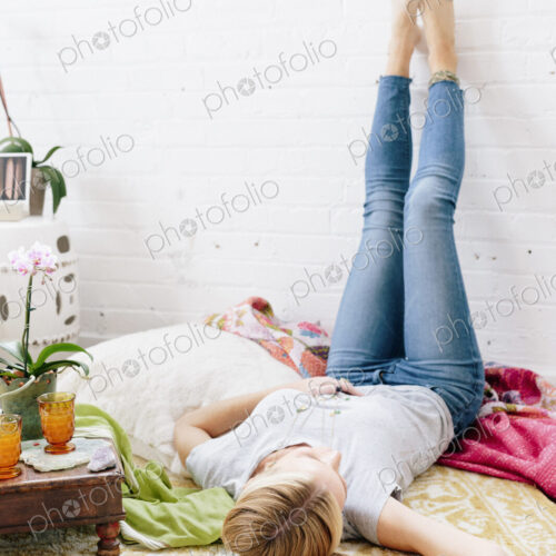 A young woman in jeans lyng on her back with her legs against the wall.