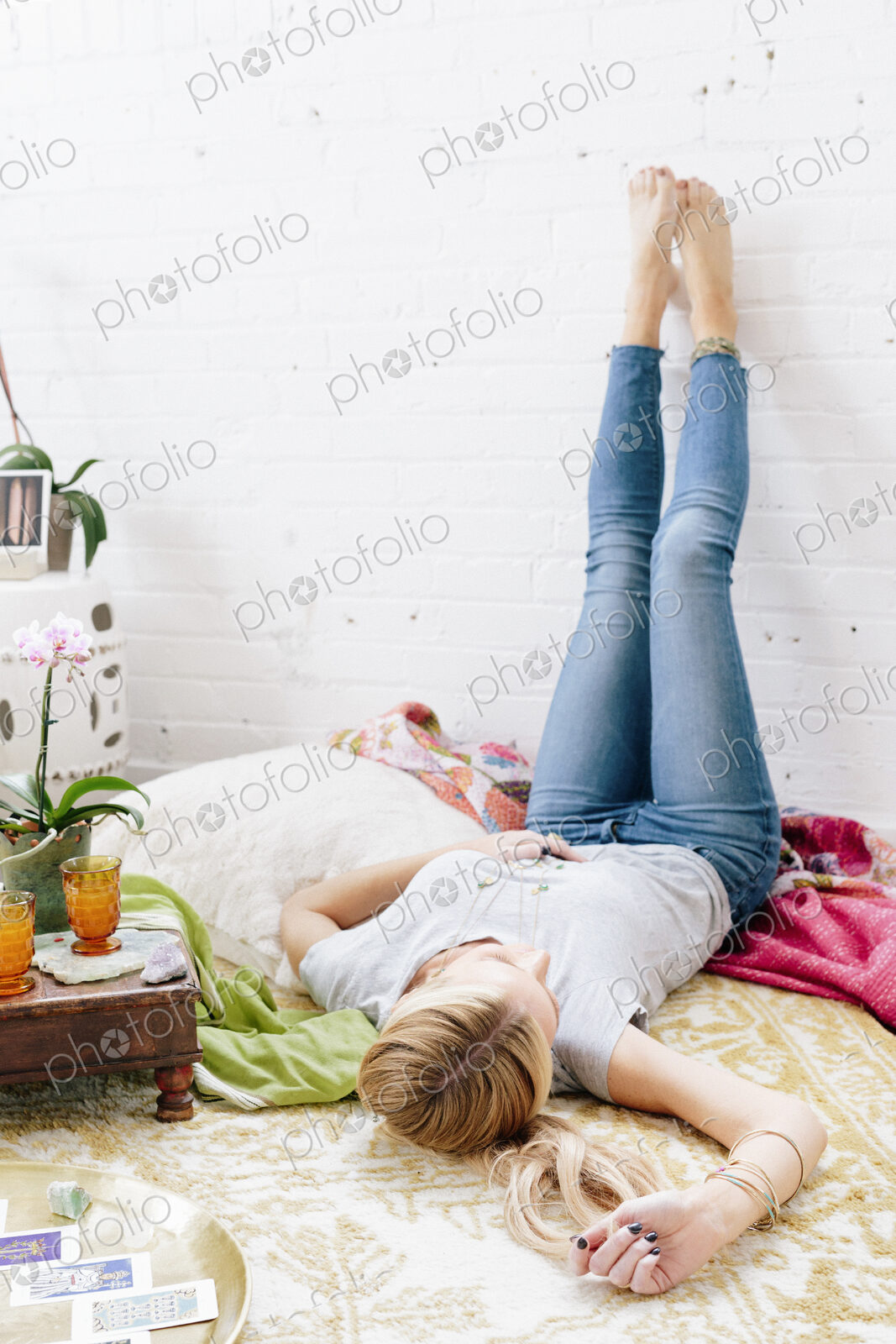 A young woman in jeans lyng on her back with her legs against the wall.