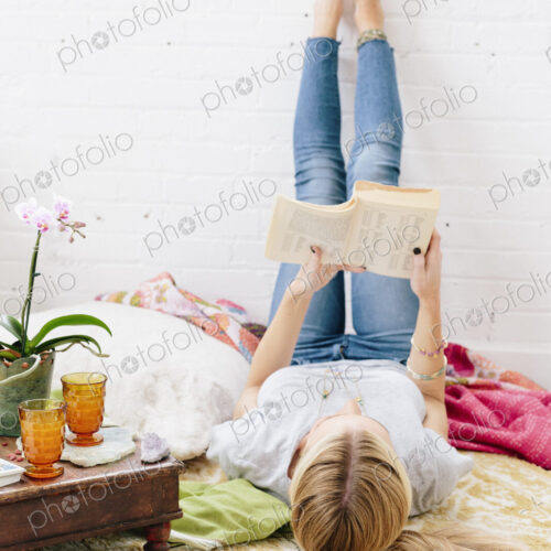 A young woman in jeans lyng on her back with her legs against the wall.