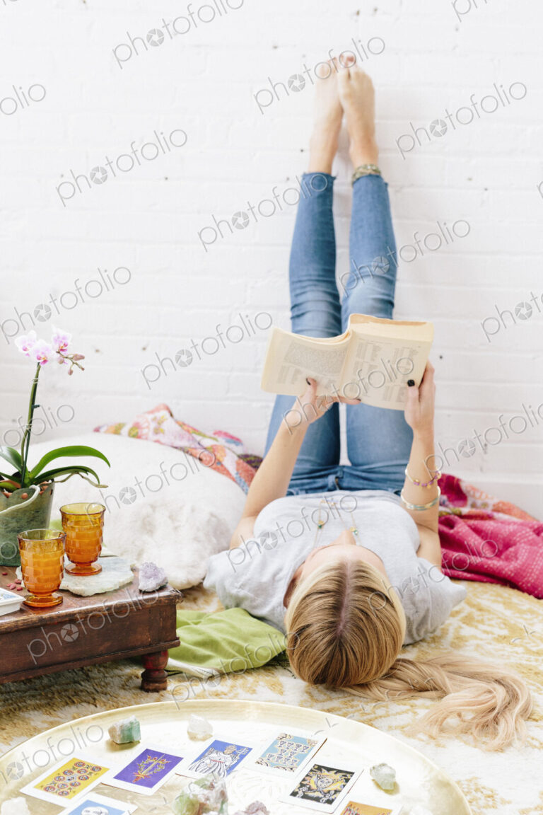 A young woman in jeans lyng on her back with her legs against the wall.