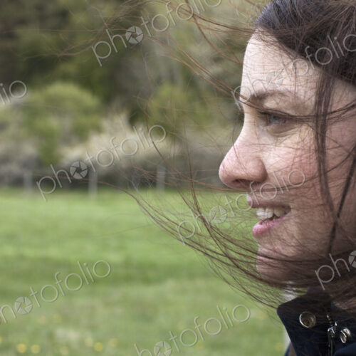 A young woman in profile. Her brown hair blowing about her face. Outdoors. Spring. A young woman in profile. Her brown hair blowing about her face. Outdoors. Spring.