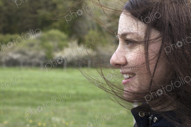 A young woman in profile. Her brown hair blowing about her face. Outdoors. Spring.