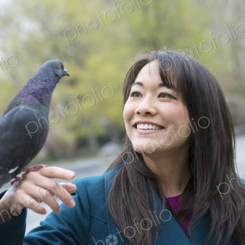 A young woman in the park with a pigeon perched on her wrist.