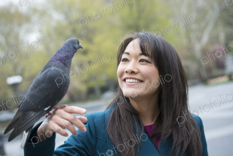 A young woman in the park with a pigeon perched on her wrist.