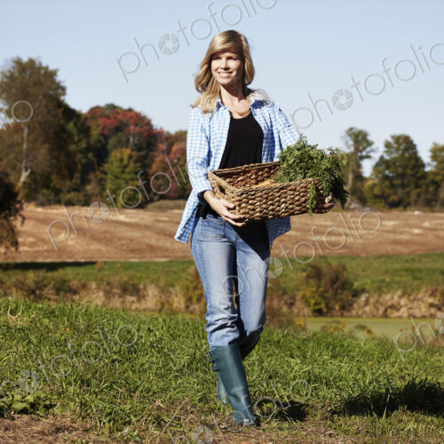 A young woman in working clothes walking across a field, holding a basket of crops. A young woman in working clothes walking across a field, holding a basket of crops.