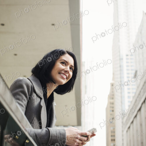 A young woman leaning over a balcony and holding a cellphone, smiling. A young woman leaning over a balcony and holding a cellphone, smiling.