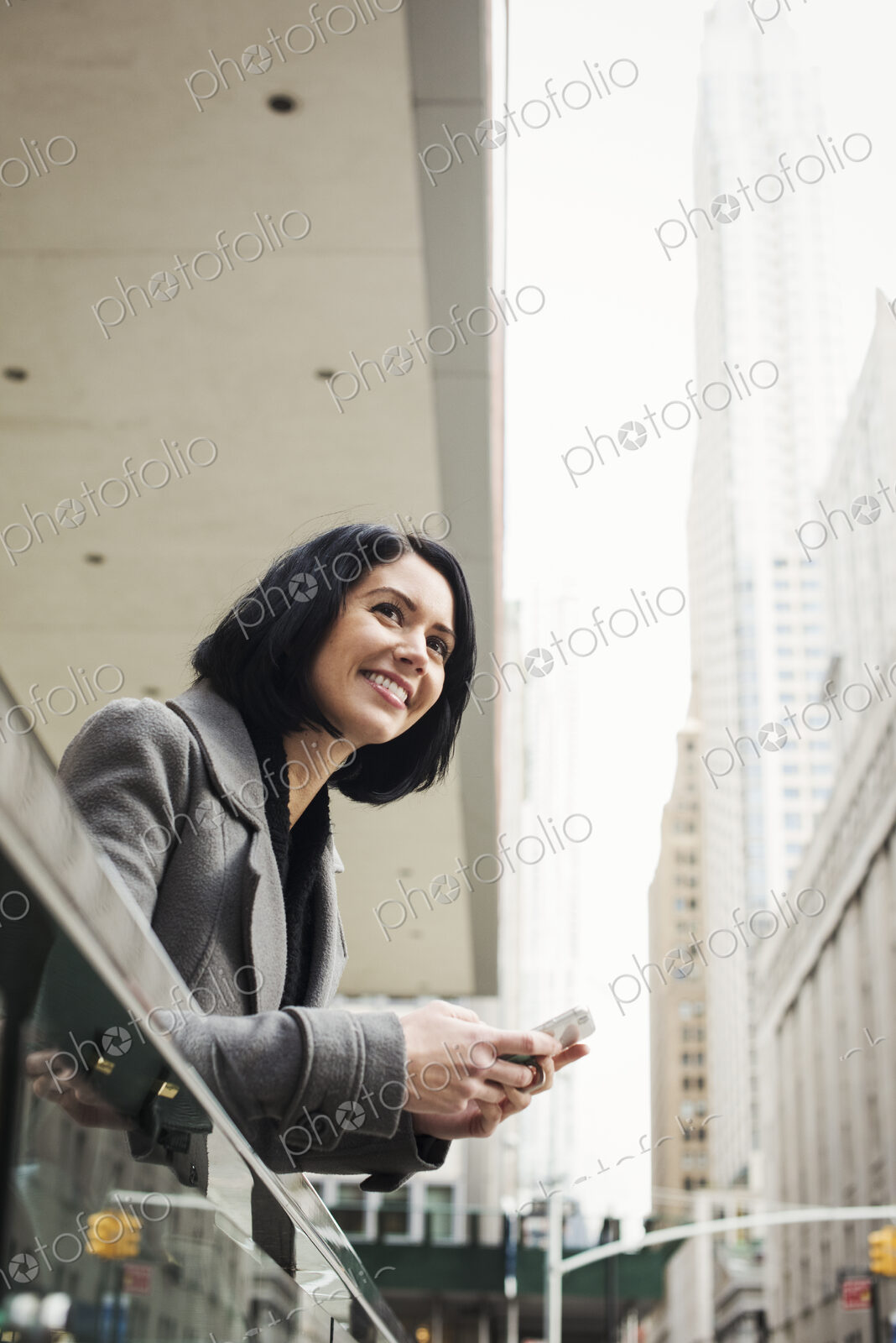 A young woman leaning over a balcony and holding a cellphone, smiling.