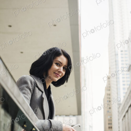 A young woman leaning over a balcony and holding a cellphone, smiling. A young woman leaning over a balcony and holding a cellphone, smiling.