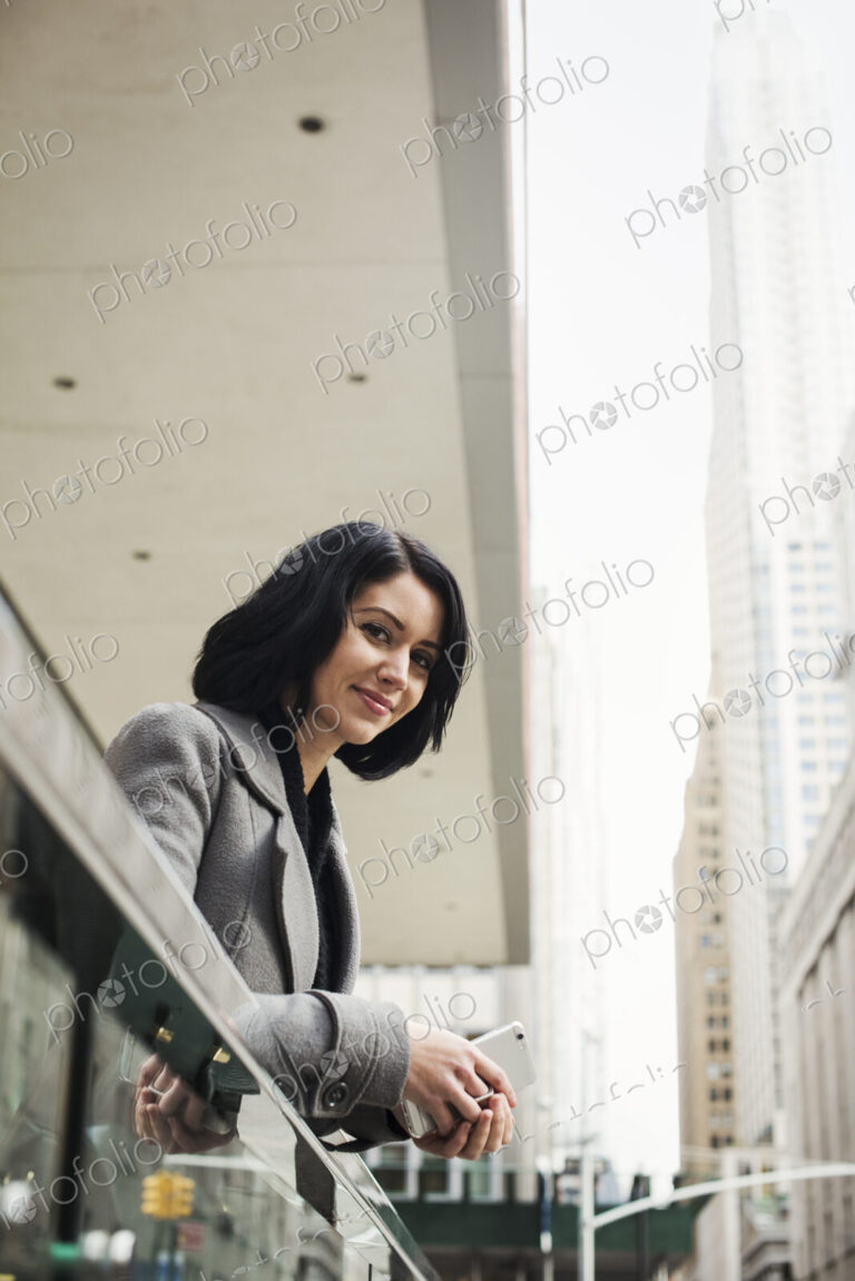 A young woman leaning over a balcony and holding a cellphone, smiling.