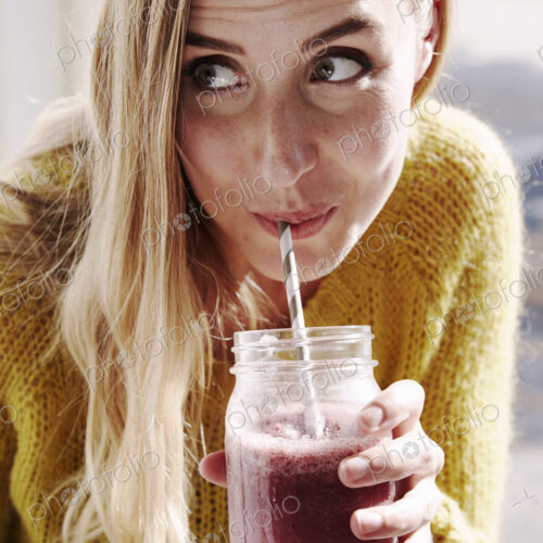 A young woman leaning over and sipping a smoothie from a straw.