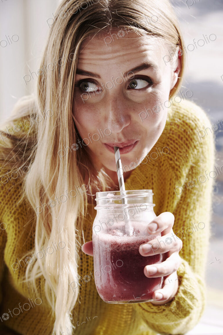 A young woman leaning over and sipping a smoothie from a straw.