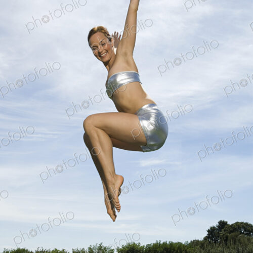 A young woman leaping in the air, knees bent and legs tucked up underneath her. Acrobat.