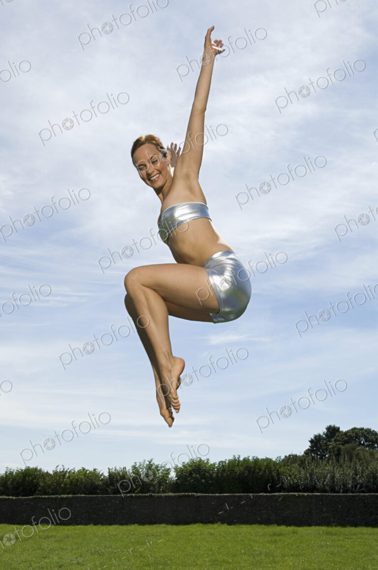 A young woman leaping in the air, knees bent and legs tucked up underneath her. Acrobat.