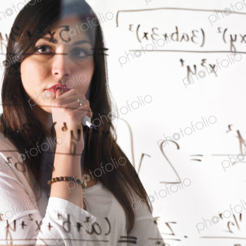 A young woman looking at a mathematical equation written out with black marker on a…