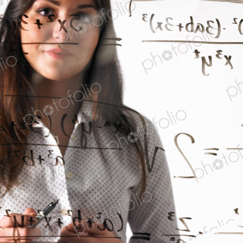A young woman looking at a mathematical equation written out with black marker on a…