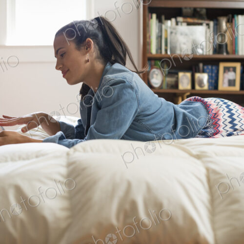 A young woman lying on her bed using a digital tablet.