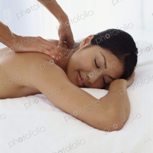 A young woman lying on her front having her shoulders massaged. A young woman lying on her front having her shoulders massaged.
