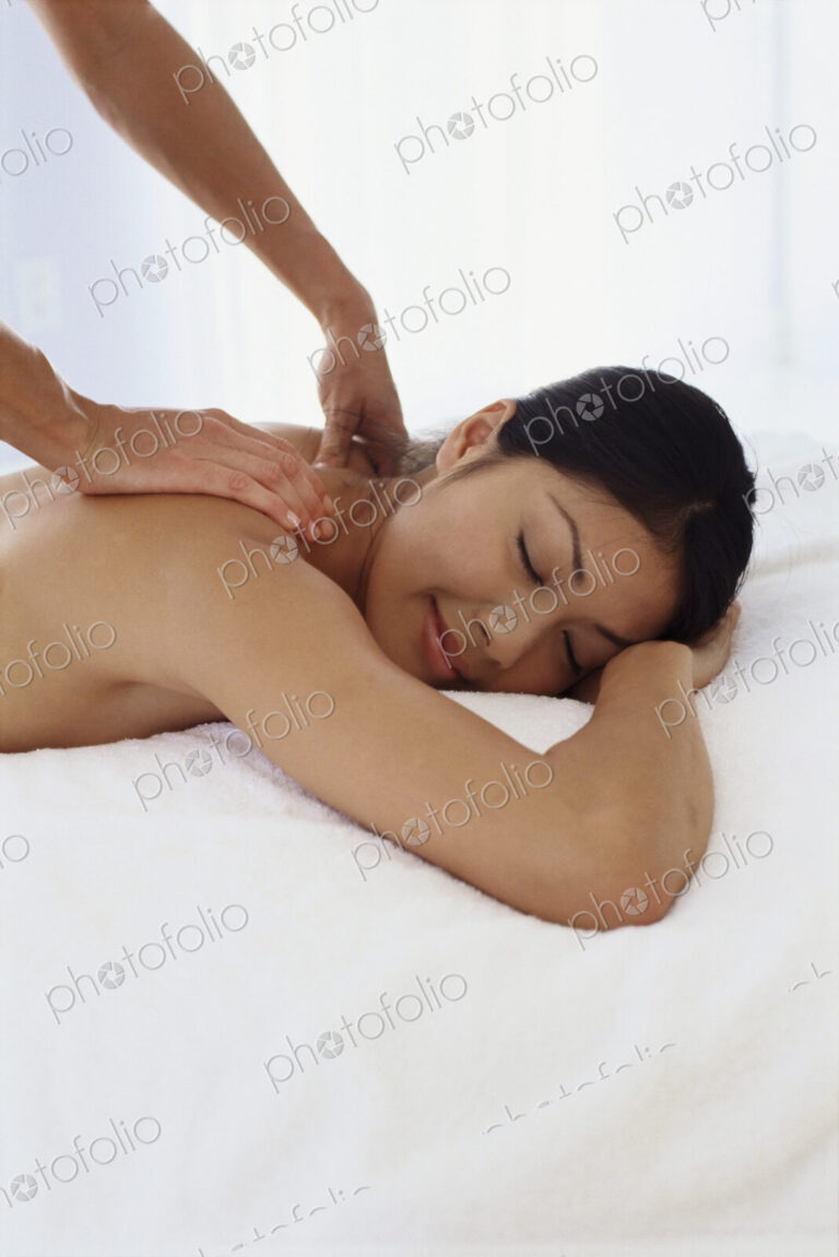 A young woman lying on her front having her shoulders massaged.