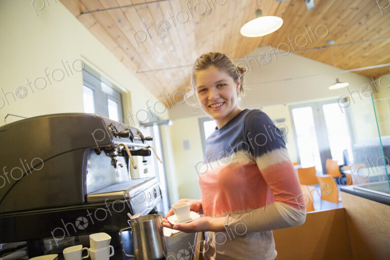A young woman making coffee using a large coffee machine.