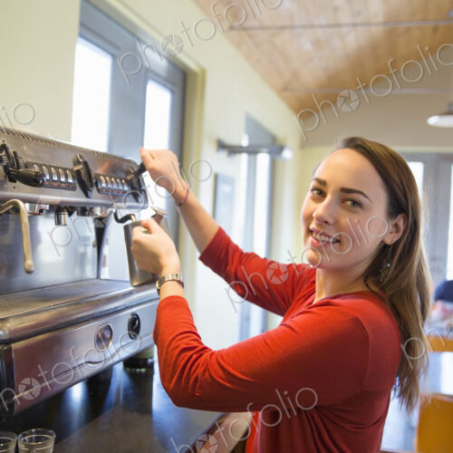 A young woman making coffee using a large coffee machine.