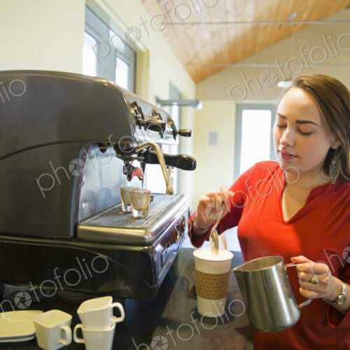 A young woman making coffee using a large coffee machine. Pouring frothed milk onto a cup. A young woman making coffee using a large coffee machine. Pouring frothed milk onto a cup.