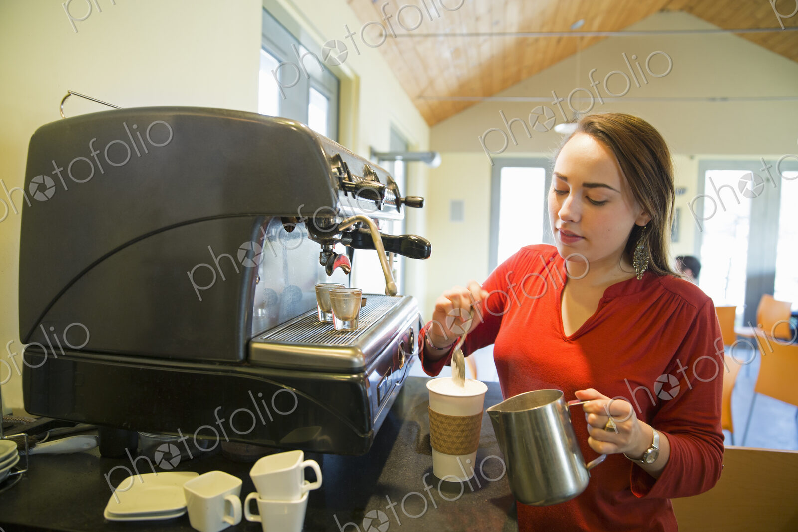 A young woman making coffee using a large coffee machine. Pouring frothed milk onto a cup.