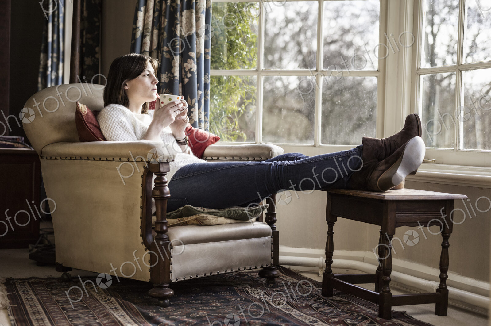 A young woman relaxing at home, with her feet up, having a cup of tea.