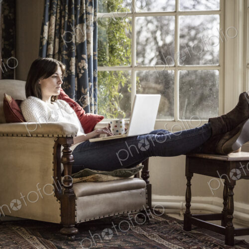 A young woman relaxing at home, with her feet up, using a laptop. A young woman relaxing at home, with her feet up, using a laptop.
