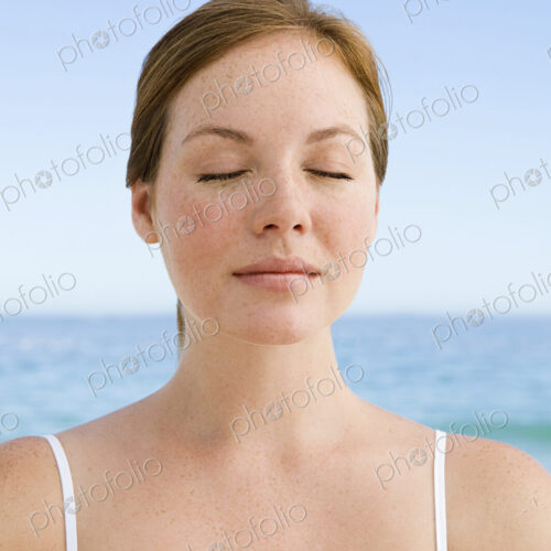 A young woman seated on the beach in a relaxed pose, with her eyes closed. A young woman seated on the beach in a relaxed pose, with her eyes closed.