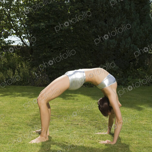A young woman showing her flexibility, leaning backwards in an arch with hands and…